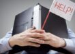 man sitting at desk with a laptop over his head while holding a sign for help
