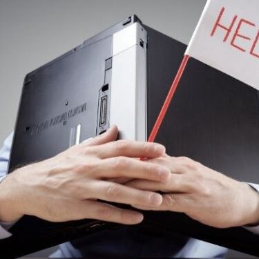 man sitting at desk with a laptop over his head while holding a sign for help