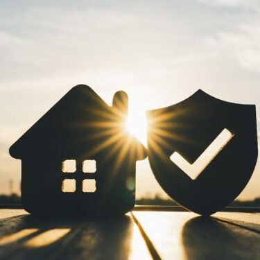 small cutout of a home on a boardwalk next to a cutout of a shield with a check mark in it