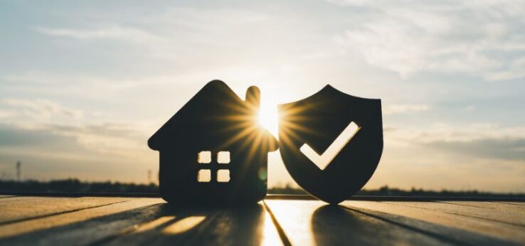 small cutout of a home on a boardwalk next to a cutout of a shield with a check mark in it