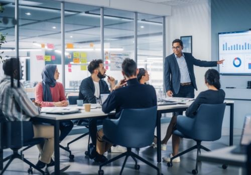 men and women in a board room going over stats on a monitor