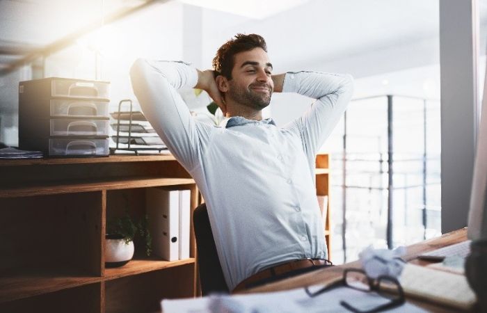 man sitting at desk with hands behind his head