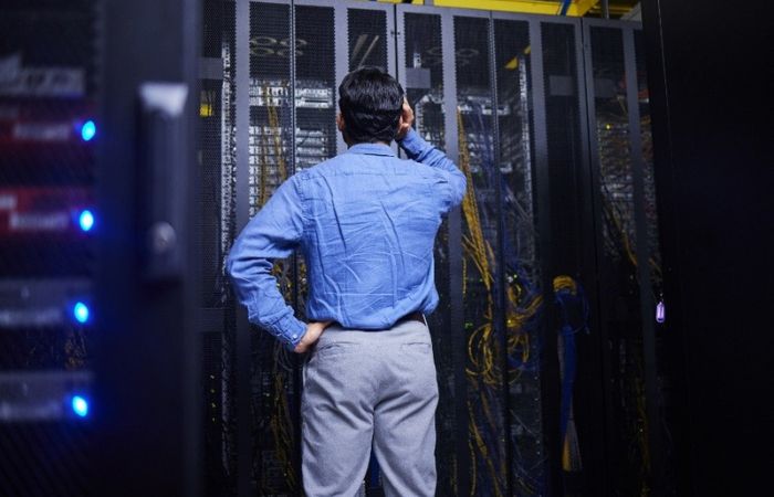 man with his back to the camera scratching his head confused, looking at the computer server